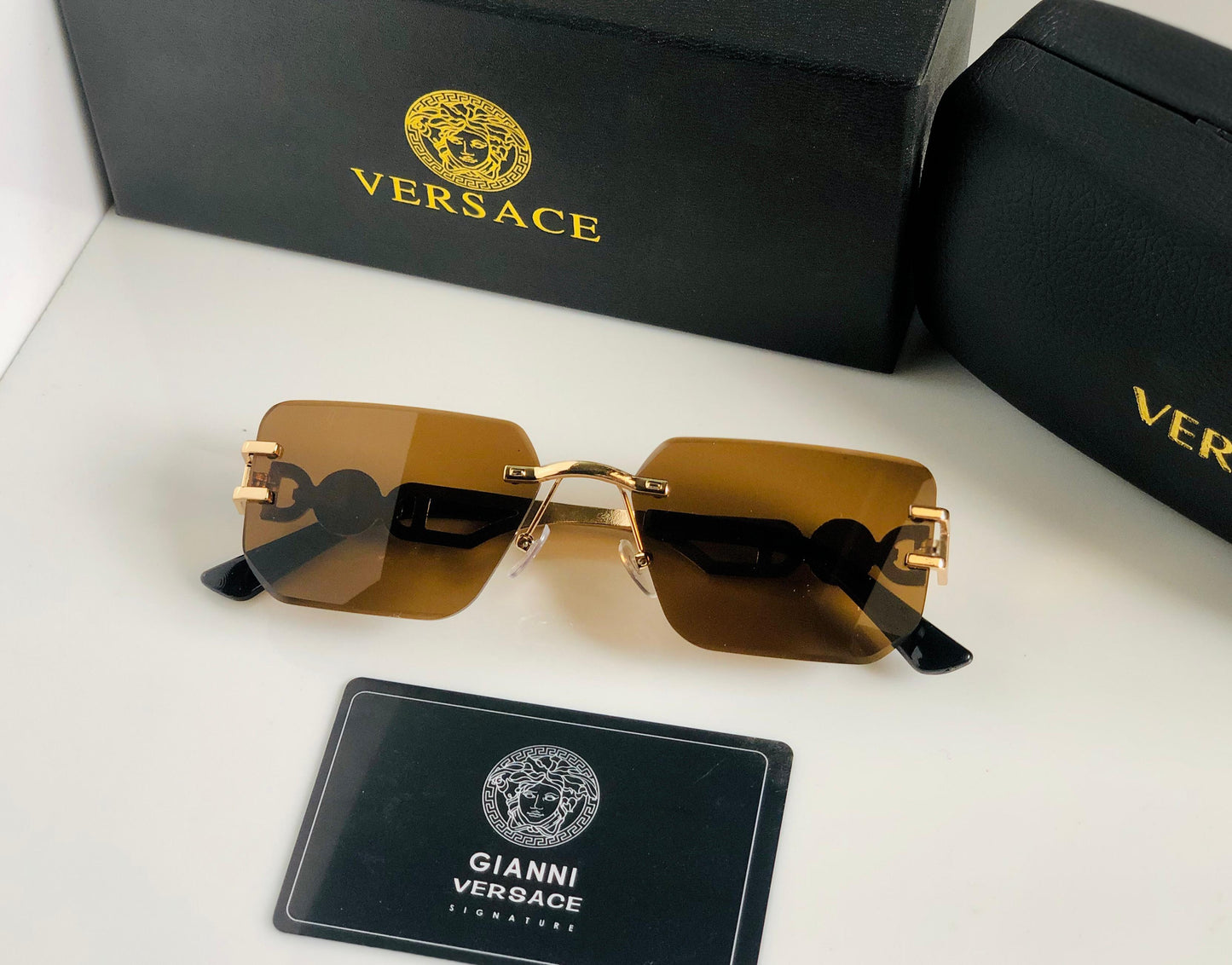 Vers ace sunglasses with gold frames and brown lenses, accompanied by a Versace box and card on a white background.
