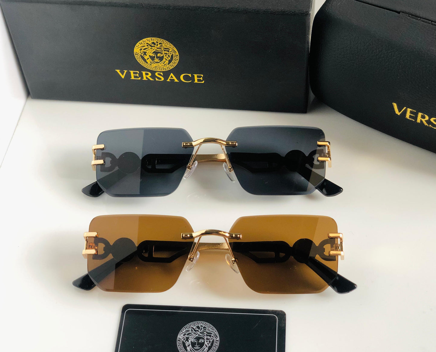 Ver sace sunglasses with gold frames and black lenses on a white surface with Versace packaging.