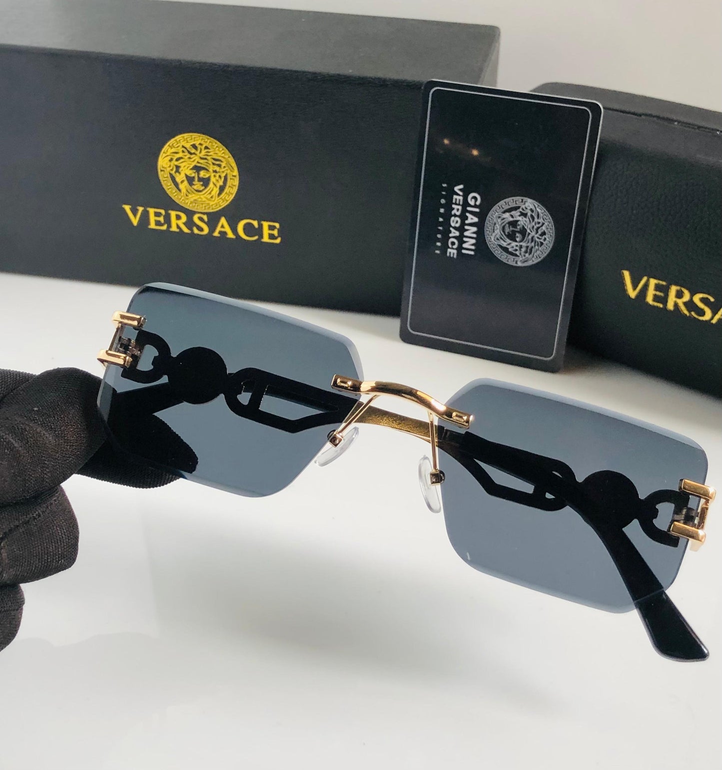 Ver sace sunglasses held by a gloved hand with Ver sace packaging in the background.