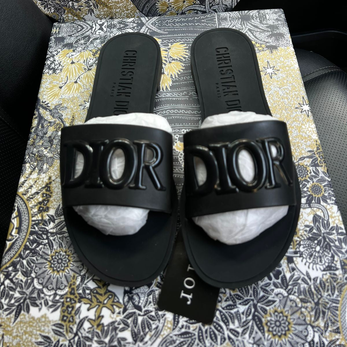 Black slides with 'Dior' logo on a patterned surface
