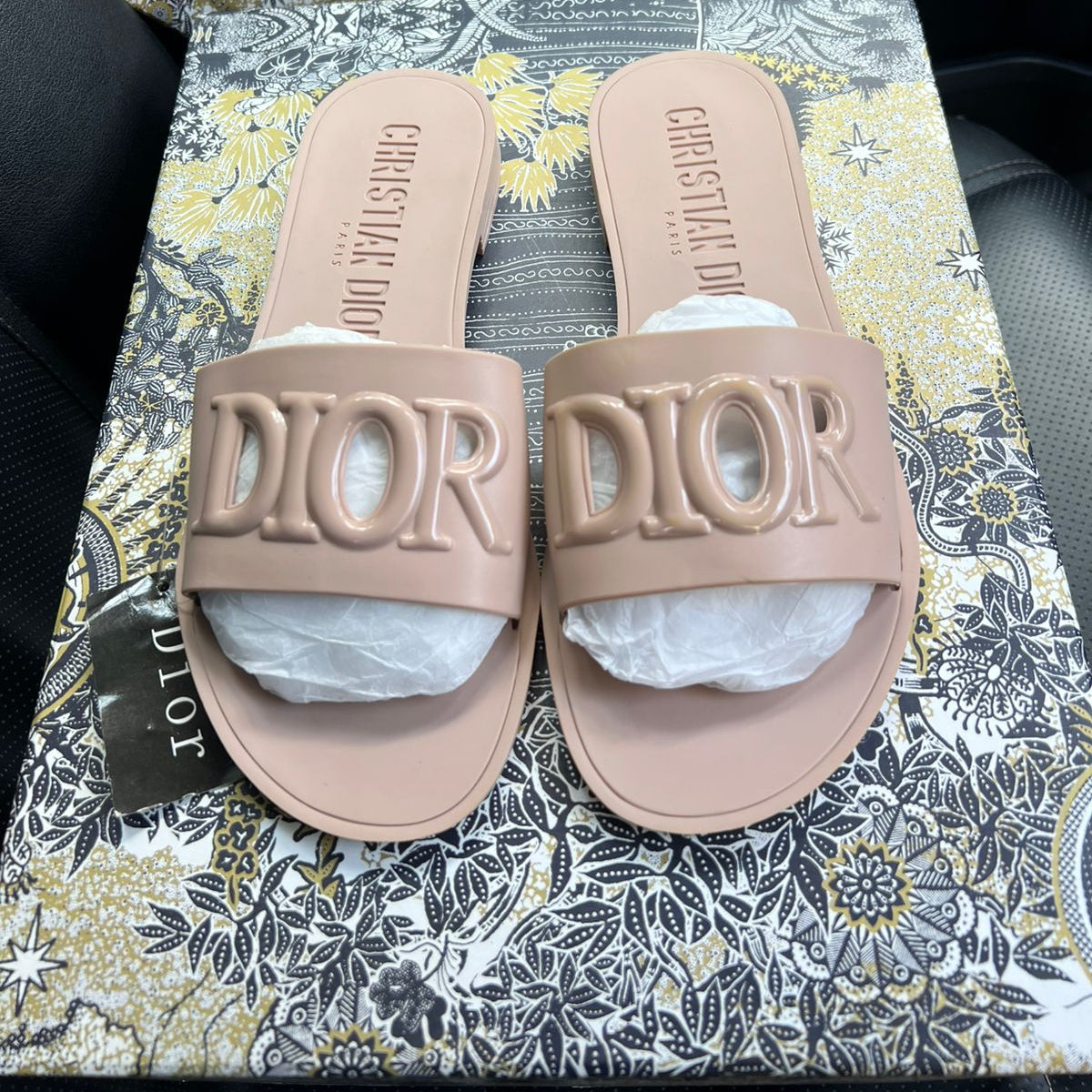 Beige Dior slides on a patterned surface with Dior branding.