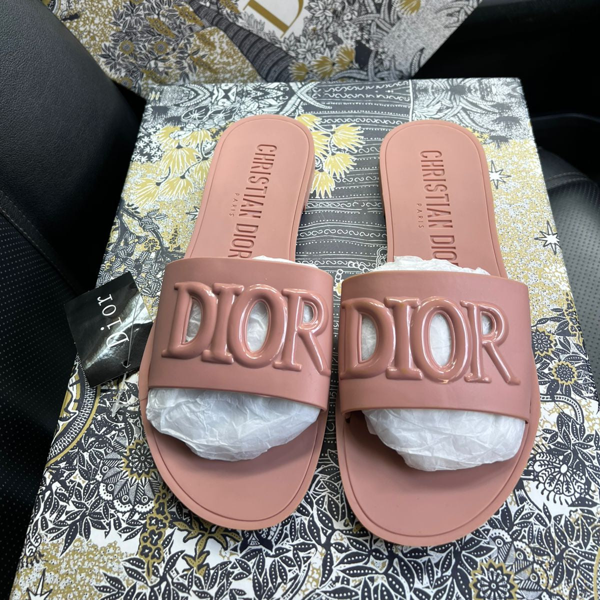Pink Dior slides on a floral-patterned surface with a Dior box in the background.