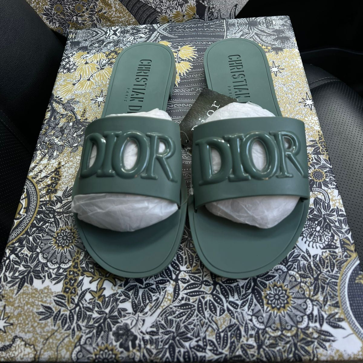 Green Dior slides on a patterned surface with a Dior box in the background.