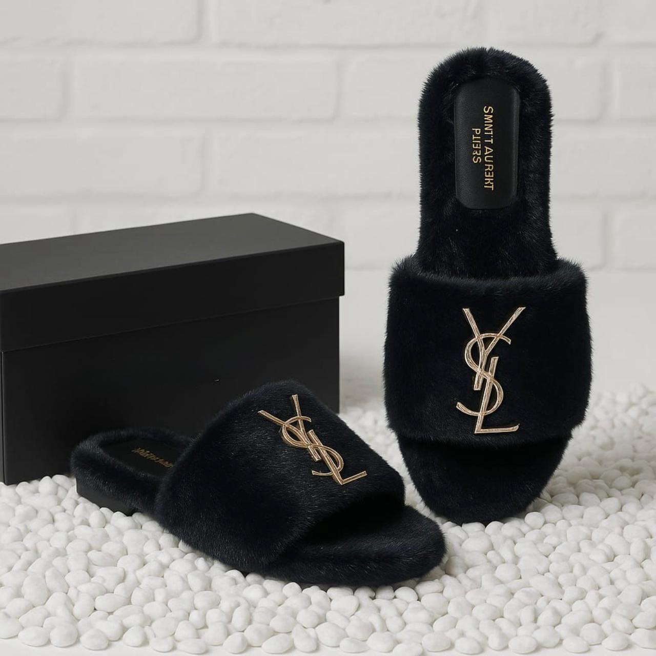 Black fuzzy slippers with Y S L logo next to a black box on a white textured surface.