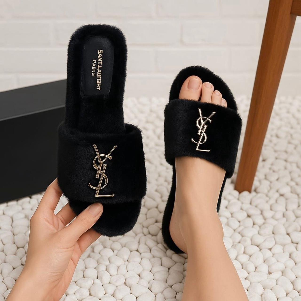 Black fur slides with Y S L logo worn by a person on a textured white surface.