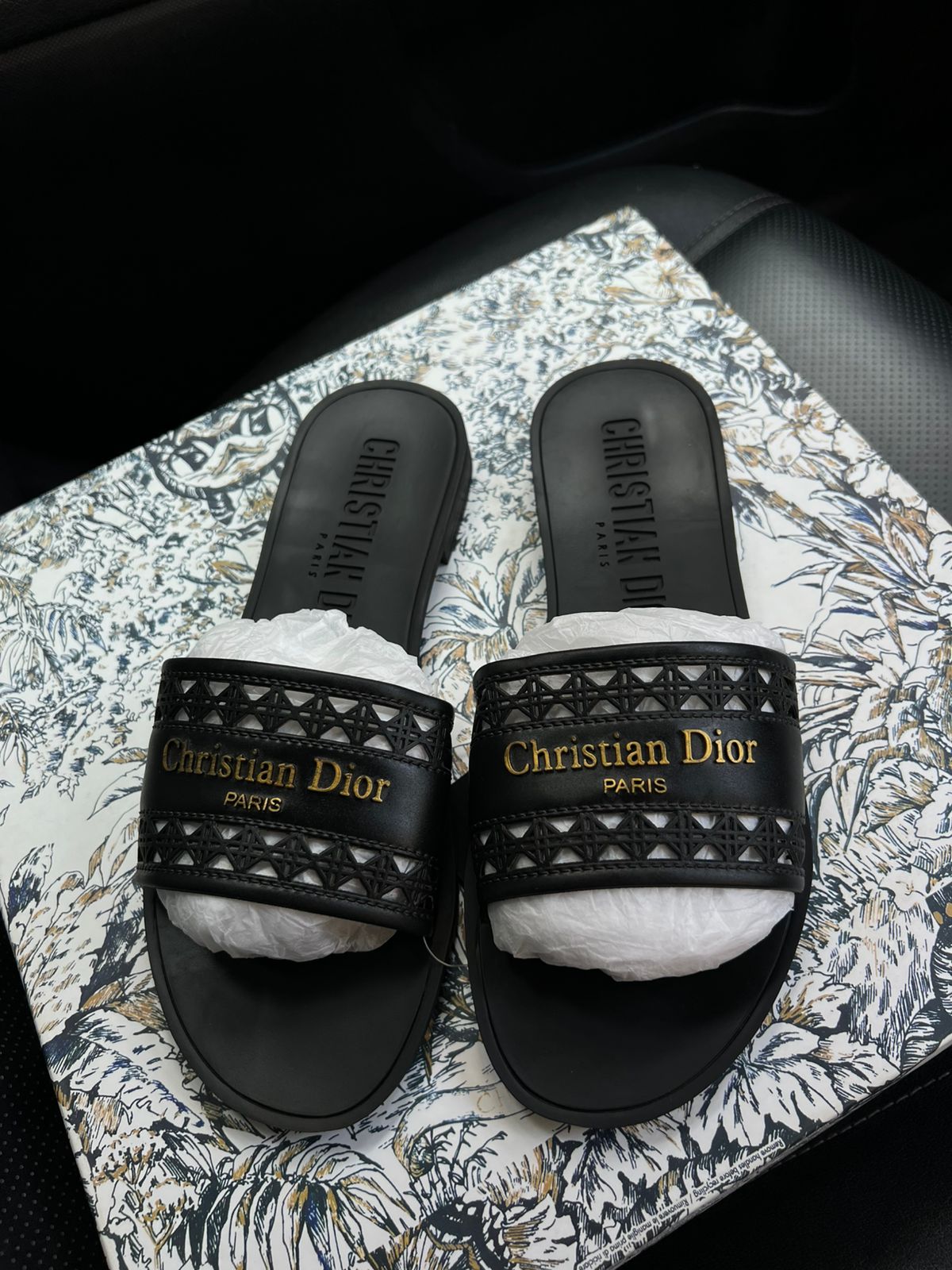 Black Christian Dior slides with white soles on a patterned surface