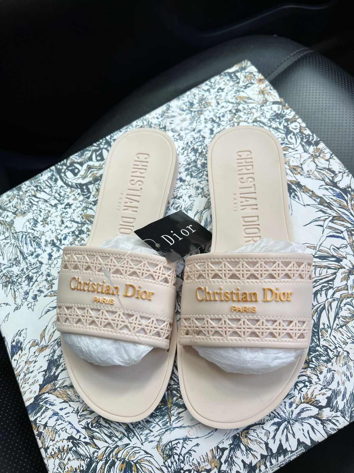 Beige Christian Dior slides with a brand tag on a patterned surface