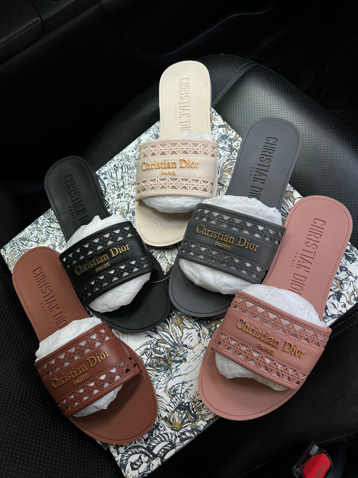 Set of Christian Dior slides in various colors on a patterned surface.